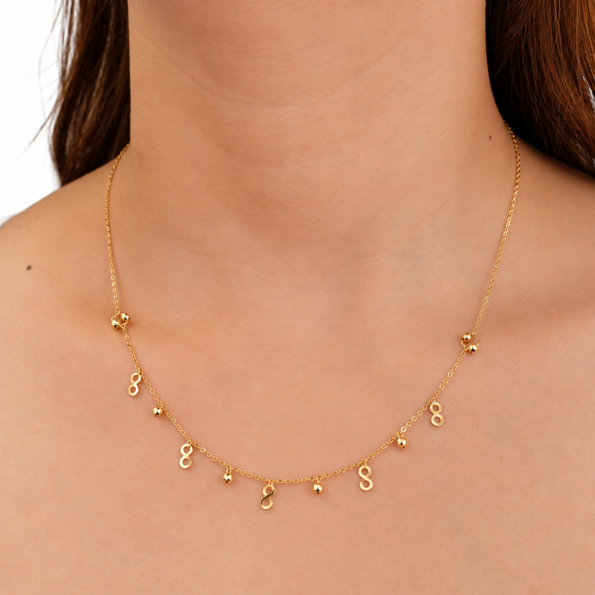 A delicate gold necklace with multiple small dangling initial charms, shown worn on a model's neck.