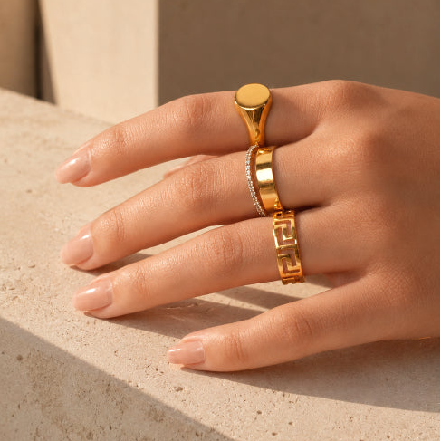 Hand wearing a gold ring on a neutral background
